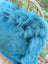 A plush teal blue faux fur throw draped over a chair back perfect for a woolly green sewing studio vibe