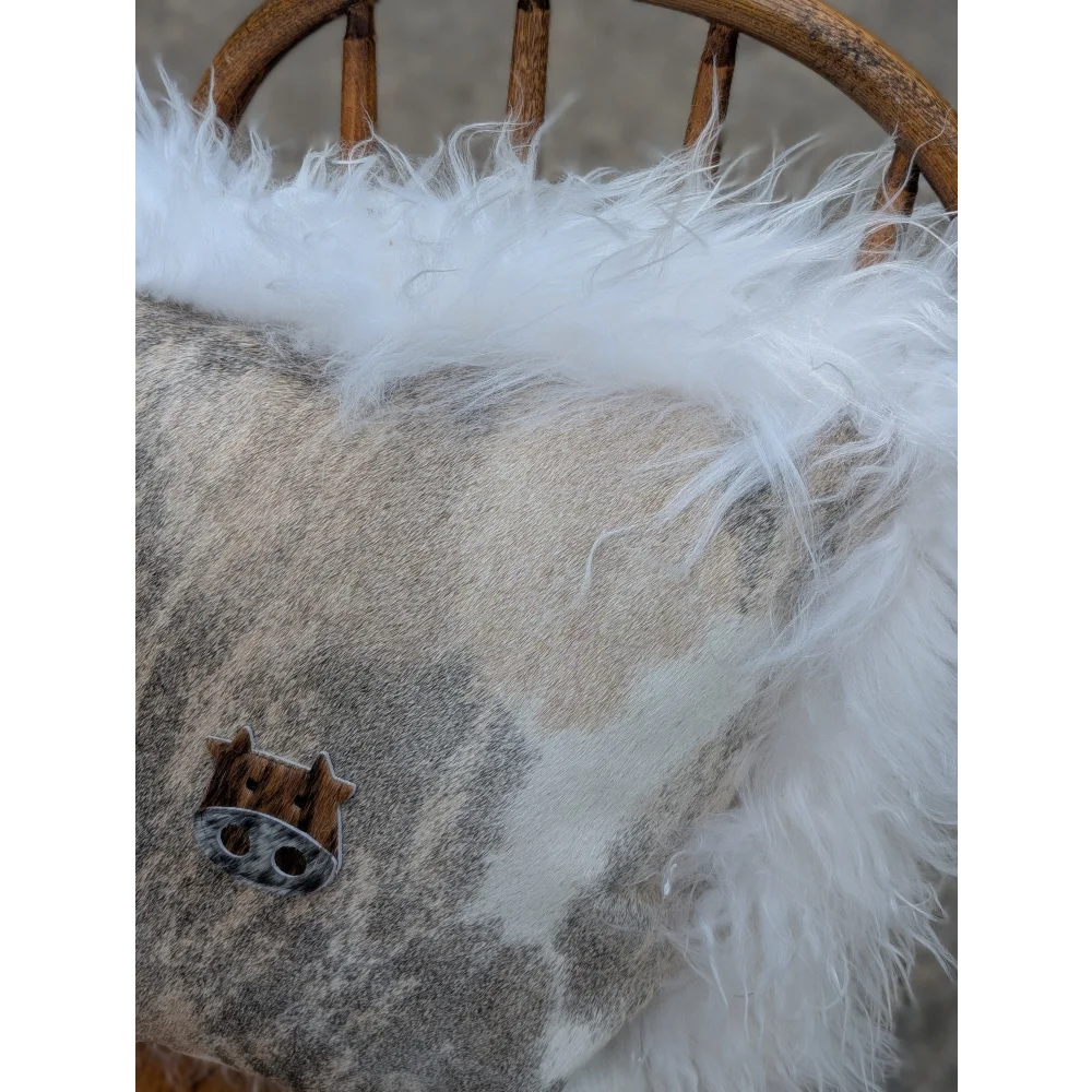 The moo cushion 2 is a cozy gray and white patterned cushion with long wool trim and a wooden pig charm