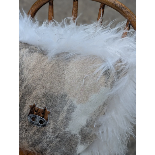 The moo cushion 2 is a cozy gray and white patterned cushion with long wool trim and a wooden pig charm