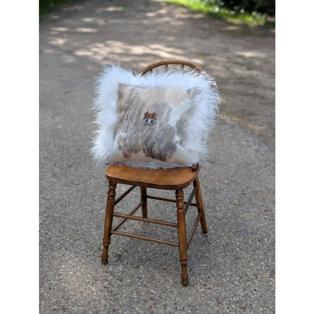 A fluffy white long wool moo cushion with gray beige cowhide pattern and embroidered cat face for cozy decor