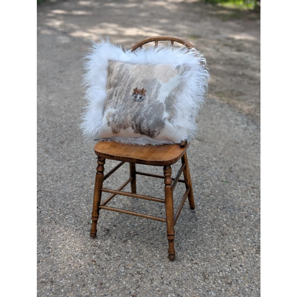 A cozy moo cushion with beige gray cowhide pattern long wool trim and embroidered cat face detail in the center