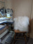 The moo cushion is a white fluffy faux fur cushion with long wool texture resting on a wooden stool by angus oliver