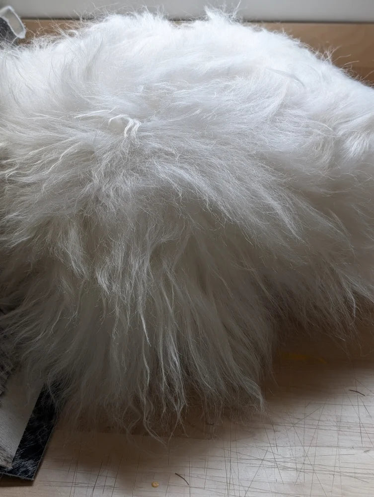 A plush white faux fur pillow named the moo cushion with long wool strands and a slightly matted texture perfect for cozy spaces