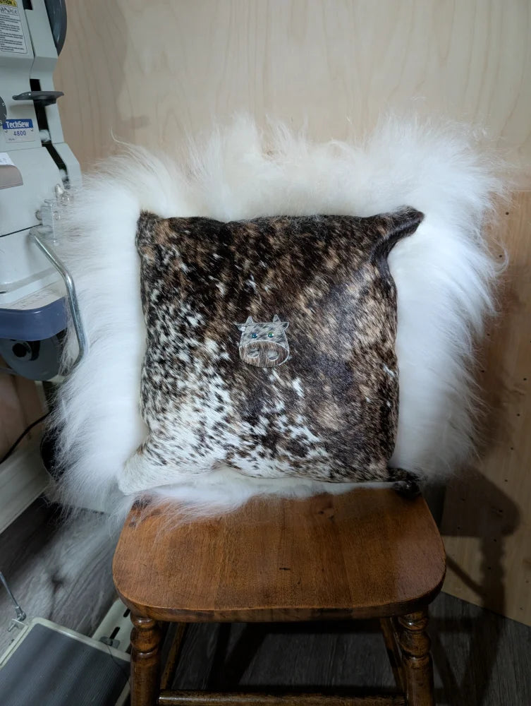 Brown and white spotted cowhide pillow called the moo cushion with a silver cat emblem embroidered using angus oliver sewing machines