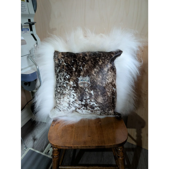 Brown and white spotted cowhide pillow called the moo cushion with a silver cat emblem embroidered using angus oliver sewing machines