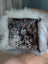 The moo cushion is a square black and white speckled cowhide pillow with plush white faux fur trim and a silver cat brooch