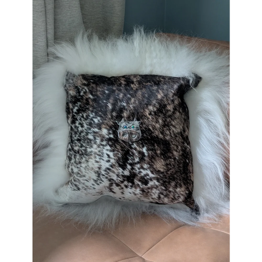 The moo cushion is a square black and white speckled cowhide pillow with plush white faux fur trim and a silver cat brooch