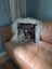 The moo cushion is a plush square pillow with a black and white speckled pattern and white faux fur trim on a tan couch