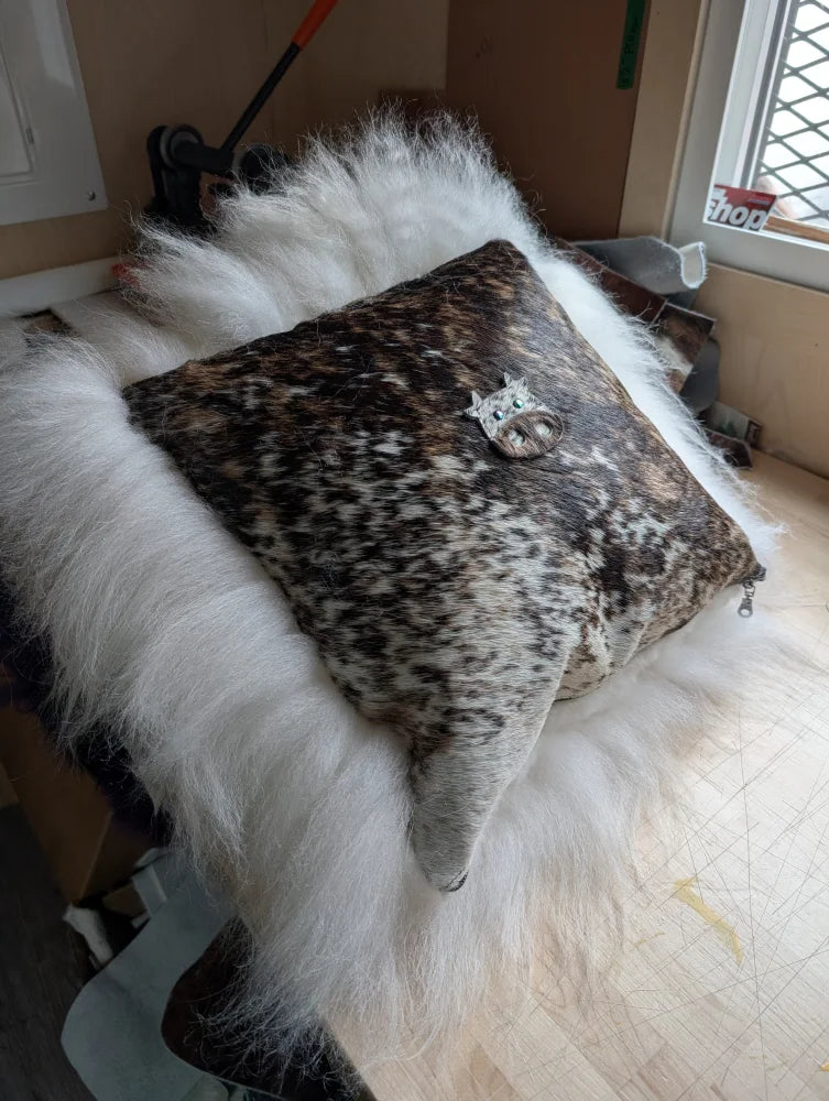 The moo cushion is a square leather cushion with brown and white spots featuring a silver cat brooch perfect for angus oliver fans