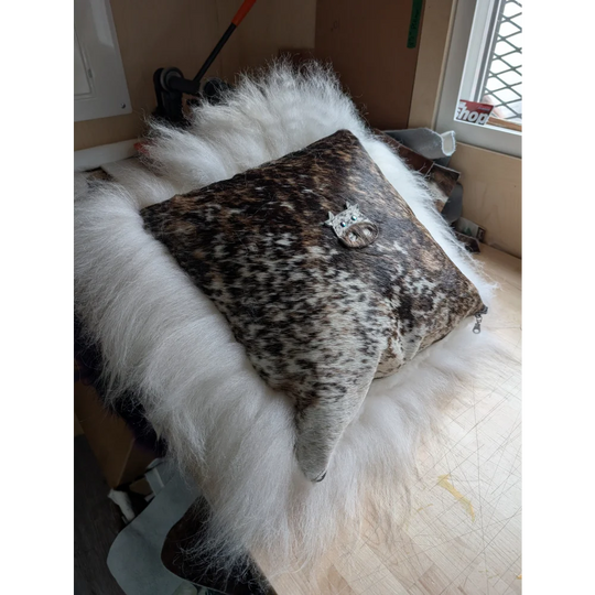 The moo cushion is a square leather cushion with brown and white spots featuring a silver cat brooch perfect for angus oliver fans