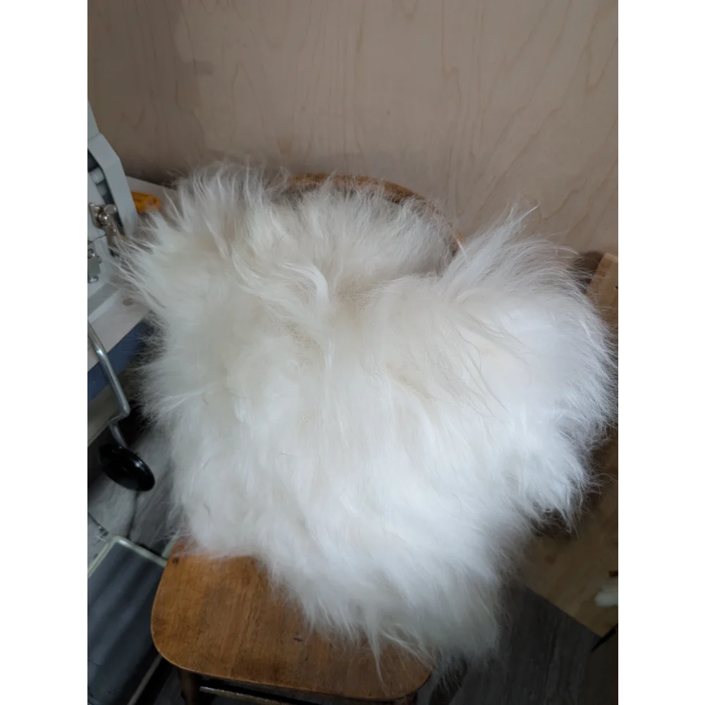 The moo cushion plush white fur throw with long wool draped over a wooden chair by angus oliver