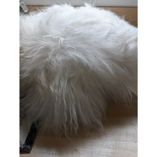 A plush white faux fur pillow named the moo cushion with long wool strands and a slightly matted texture perfect for cozy spaces