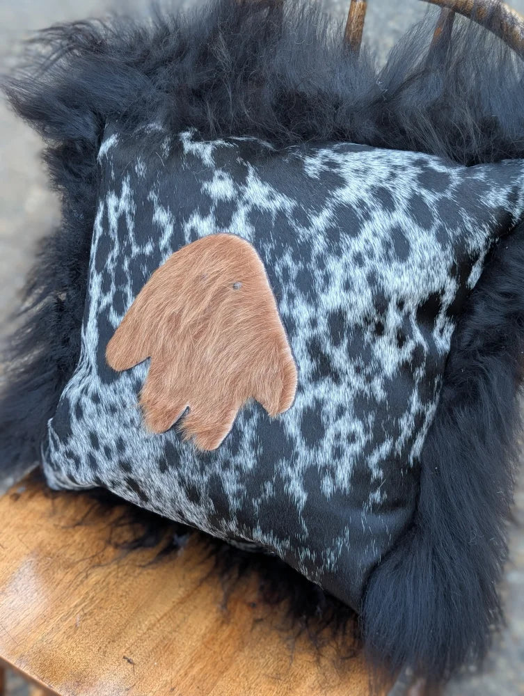 The yeti cushion cowhide pillow with black and white pattern features a brown hand-shaped leather patch and black long wool faux fur frame