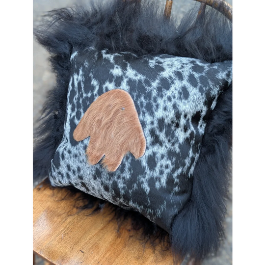 The yeti cushion cowhide pillow with black and white pattern features a brown hand-shaped leather patch and black long wool faux fur frame