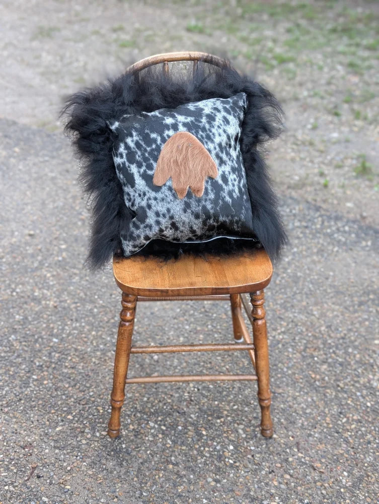Black and white spotted pillow with tan paw print appliqué draped in fluffy black long wool icelandic sheepskin