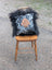 Black and white spotted pillow with tan paw print appliqué draped in fluffy black long wool icelandic sheepskin