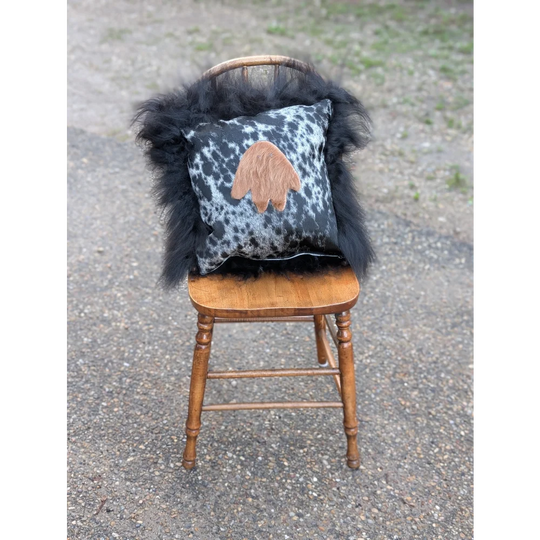 Black and white spotted pillow with tan paw print appliqué draped in fluffy black long wool icelandic sheepskin