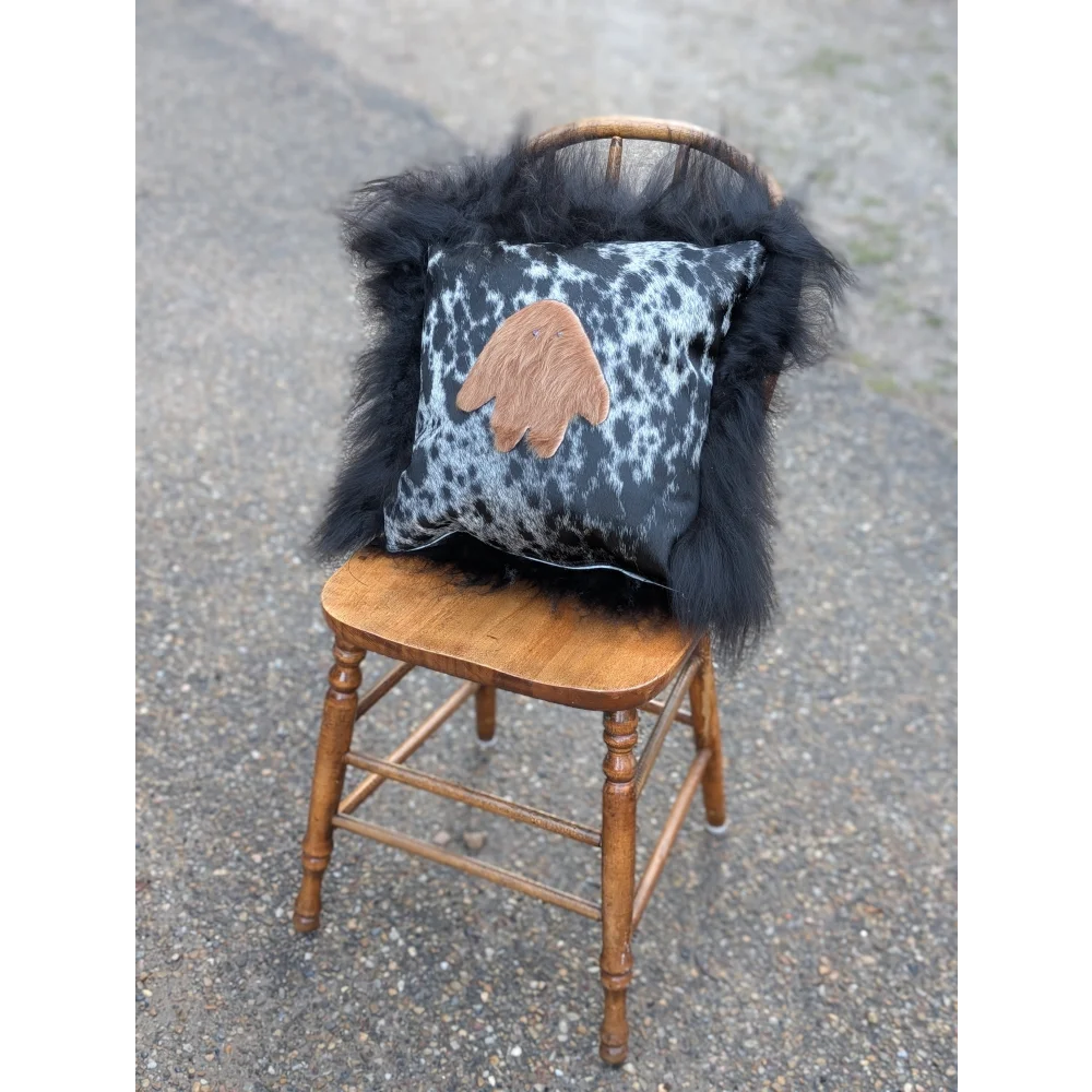 Black and white spotted yeti cushion with tan hand patch framed by black long wool icelandic sheepskin detail