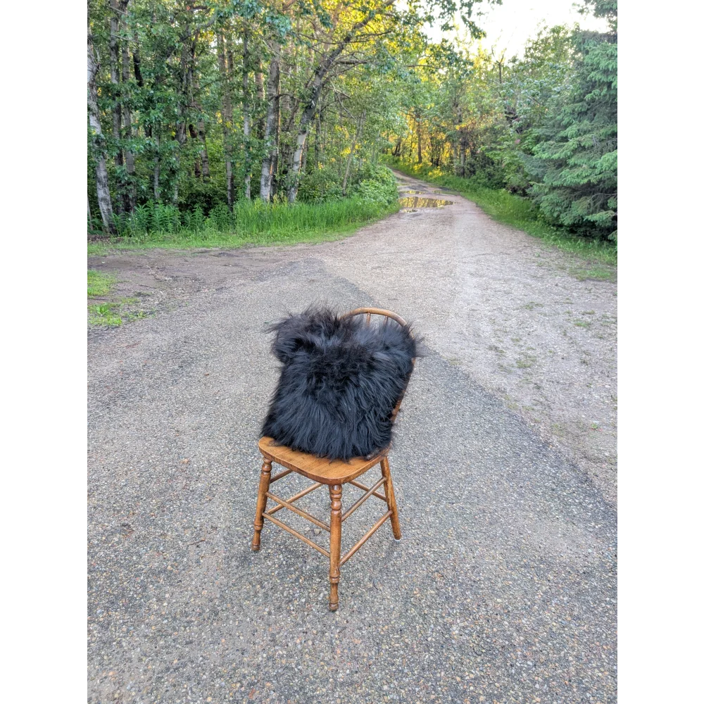A plush natural black icelandic sheepskin fur throw with long wool draped over a rustic wooden chair perfect for cozying up