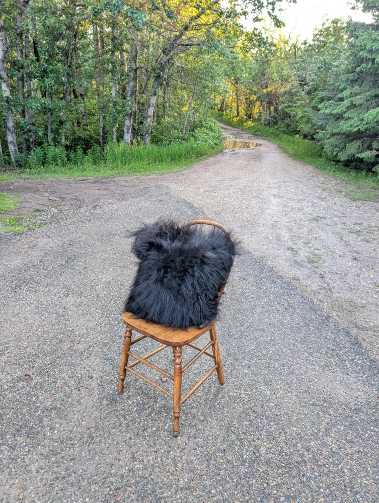 A plush natural black icelandic sheepskin fur throw with long wool draped over a rustic wooden chair perfect for cozying up