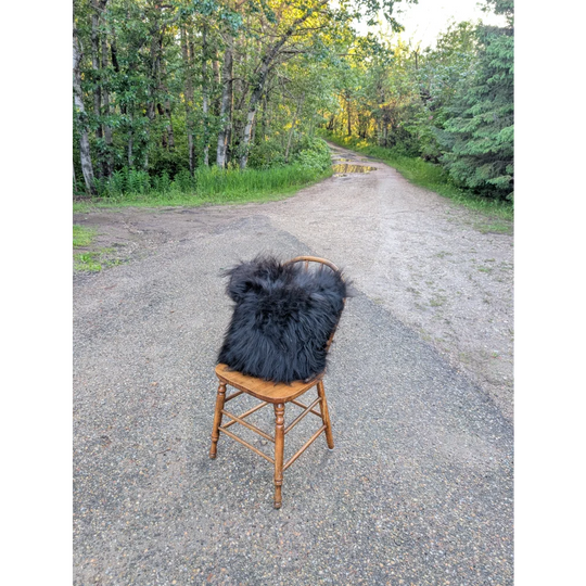 A plush natural black icelandic sheepskin fur throw with long wool draped over a rustic wooden chair perfect for cozying up