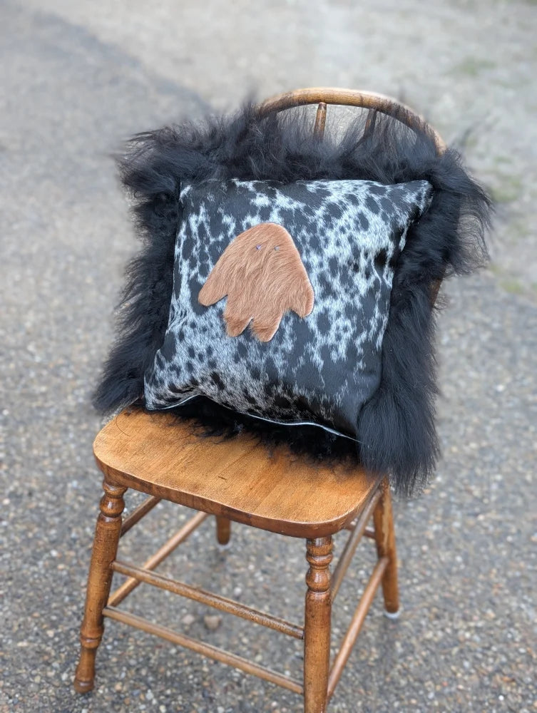 The yeti cushion icelandic sheepskin pillow with black and white spotted cowhide and tan hand patch with long wool trim