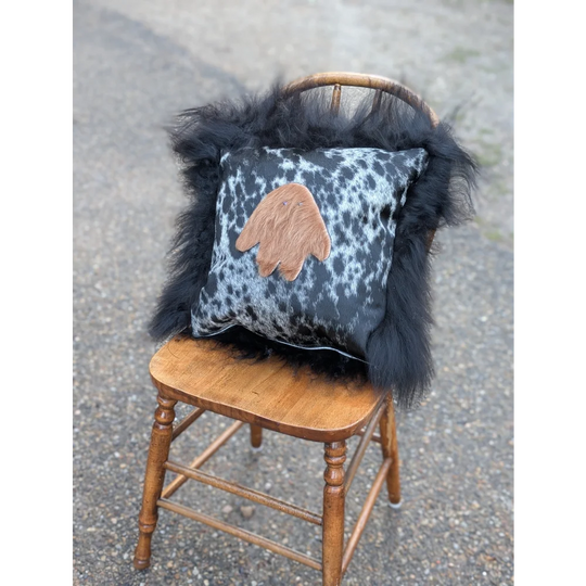 The yeti cushion icelandic sheepskin pillow with black and white spotted cowhide and tan hand patch with long wool trim