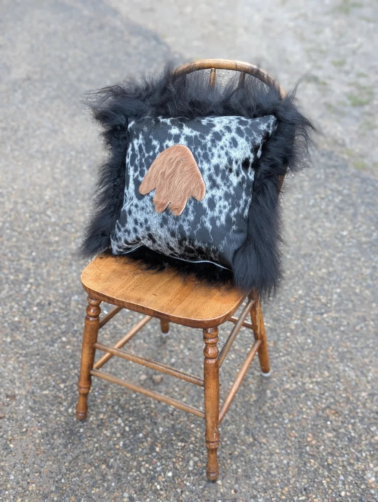 The yeti cushion cowhide icelandic sheepskin pillow with black white spots and tan hand patch framed by long wool fur