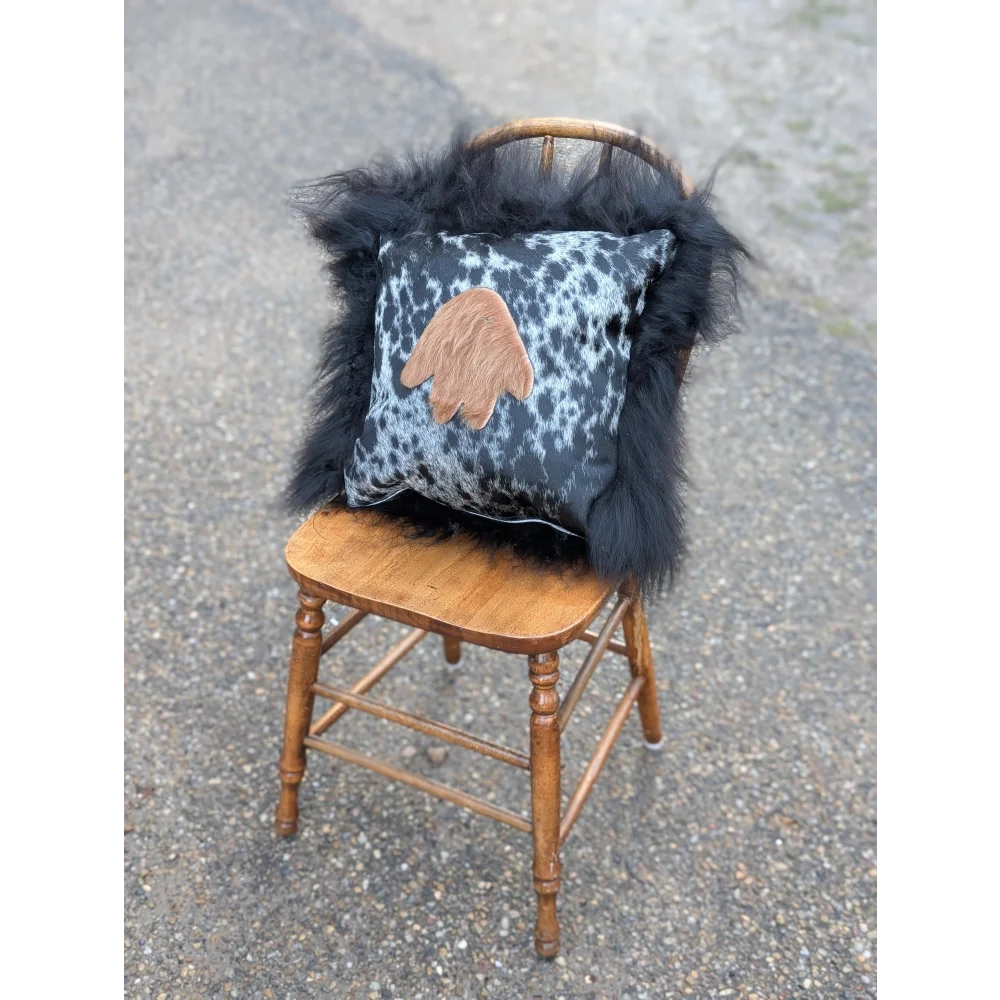 The yeti cushion cowhide icelandic sheepskin pillow with black white spots and tan hand patch framed by long wool fur