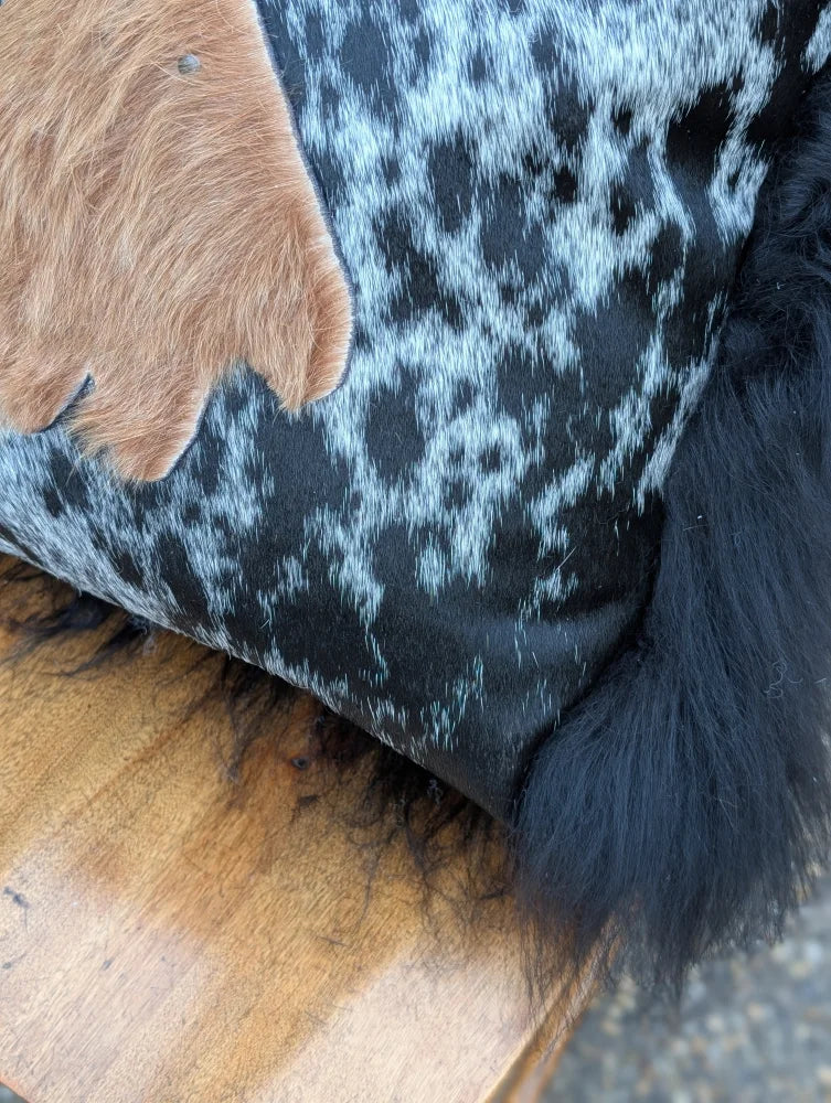 The yeti cushion cowhide pillow features black and white spots with a brown fur patch and black icelandic sheepskin trim