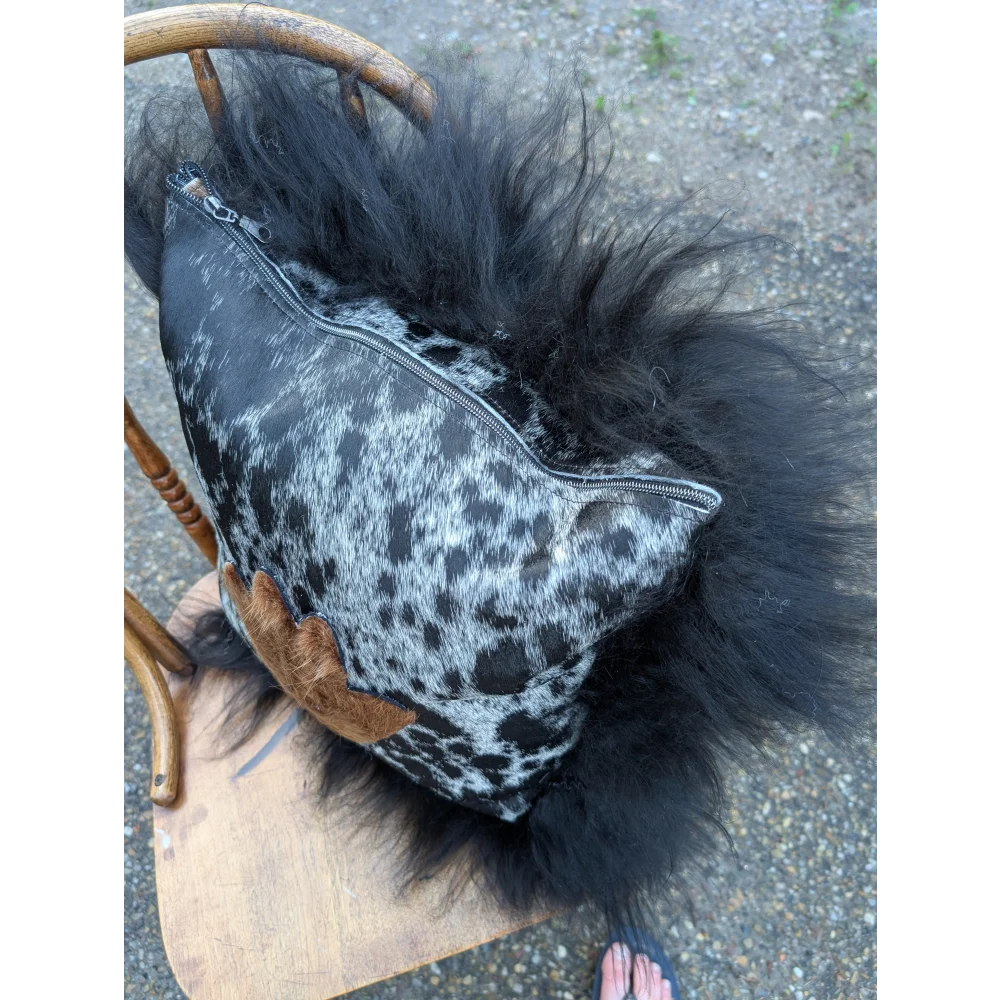 The yeti cushion cowhide pillow features black and white spots with fluffy black icelandic sheepskin trim
