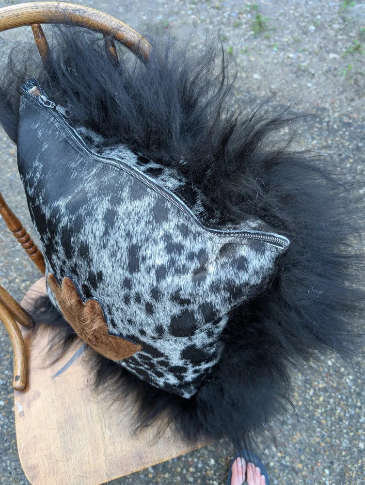 The yeti cushion cowhide pillow features black and white spots with fluffy black icelandic sheepskin trim