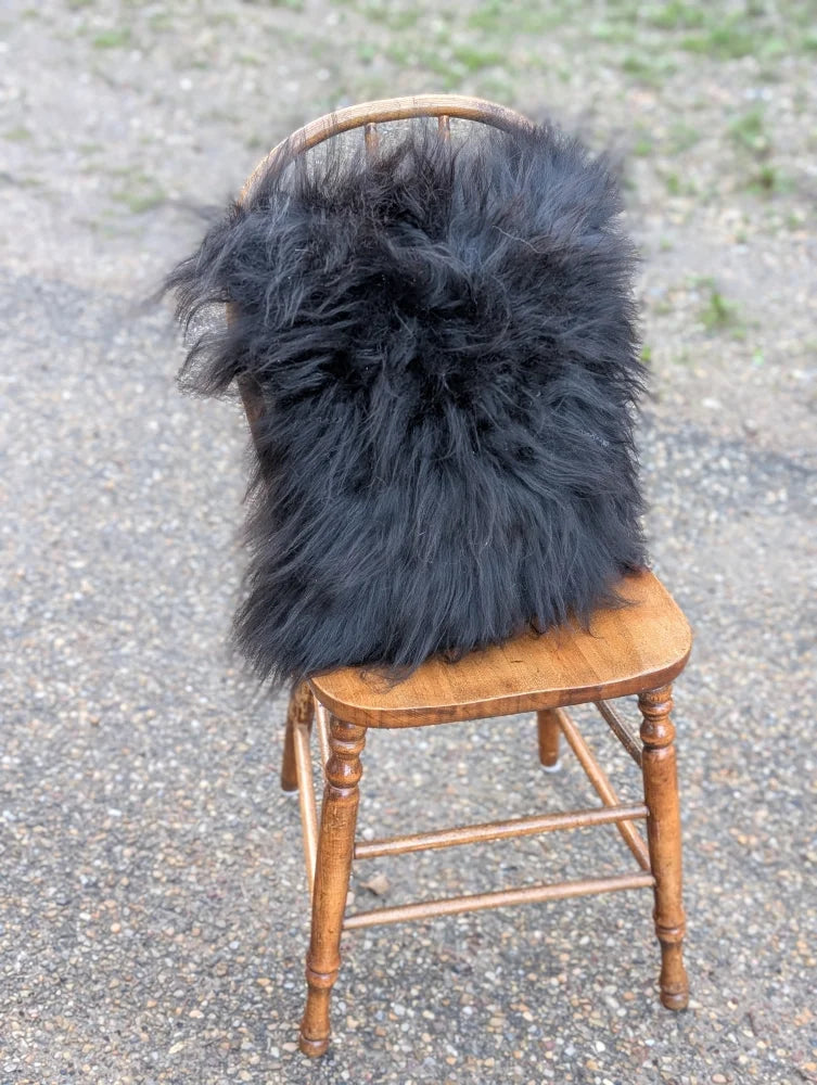 Black fluffy long wool icelandic sheepskin throw draped over wooden chair from the yeti cushion cowhide collection