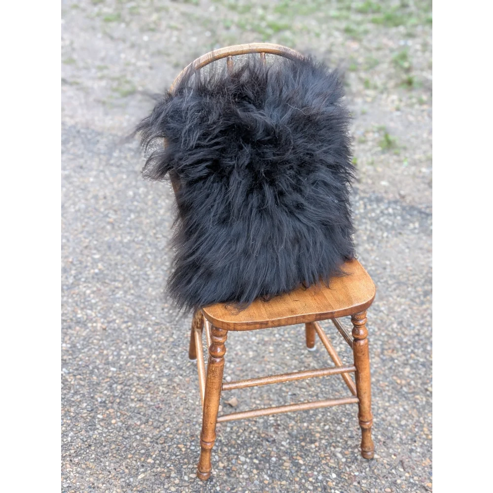 Black fluffy long wool icelandic sheepskin throw draped over wooden chair from the yeti cushion cowhide collection