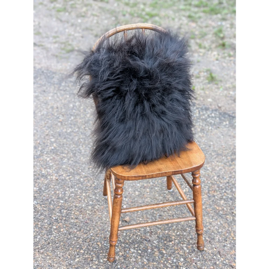 Black fluffy long wool icelandic sheepskin throw draped over wooden chair from the yeti cushion cowhide collection