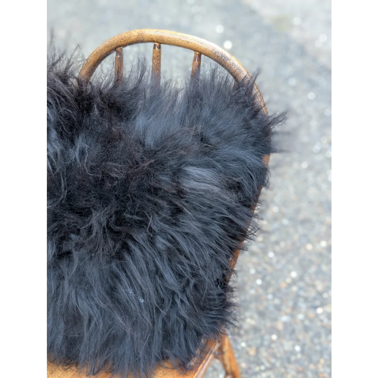Black fluffy icelandic sheepskin throw with long wool draped over wooden chair from the yeti cushion cowhide natural black collection