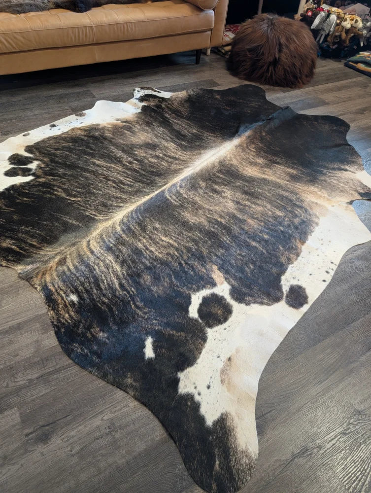 A beautiful extra large black and white cowhide rug with a textured irregular pattern laid on a wooden floor