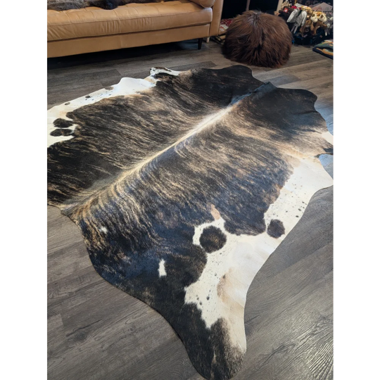 A beautiful extra large black and white cowhide rug with a textured irregular pattern laid on a wooden floor