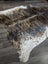 A beautiful extra large cowhide rug in natural brown and white with a textured speckled pattern perfect for large spaces