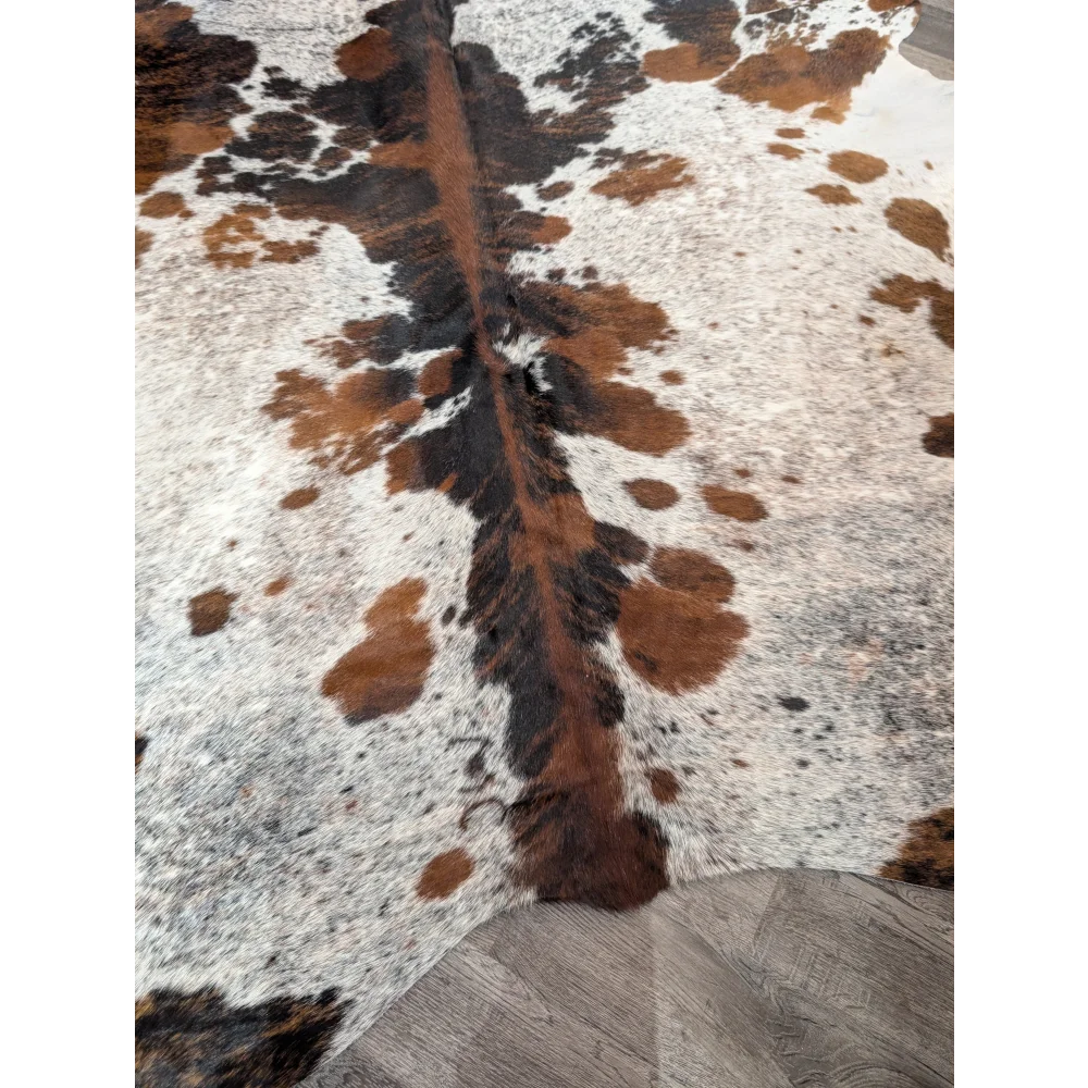 A gorgeous extra large cowhide rug with rustic charm featuring a tricolour white brown and black spotted pattern