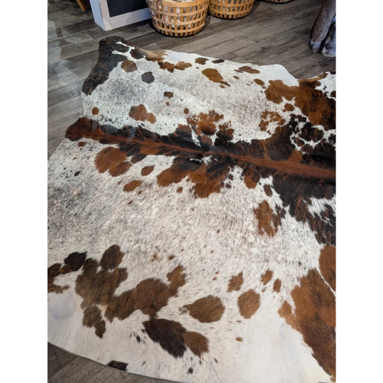 A gorgeous extra large cowhide rug with rustic charm featuring a tricolour white brown and black spotted pattern