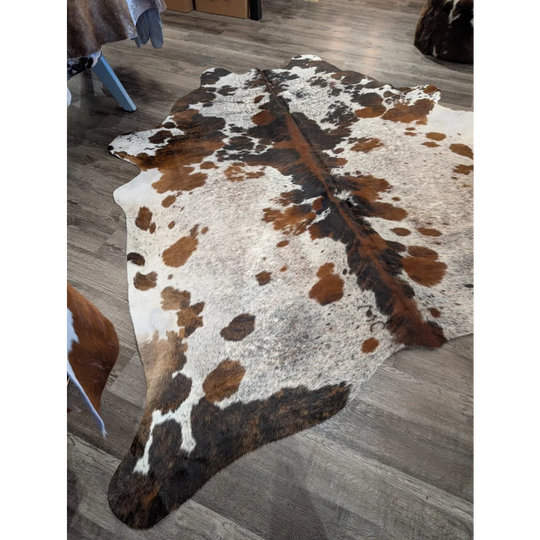A gorgeous extra large cowhide rug with a tricolour white brown and black spotted pattern adding rustic charm and unique characteristics