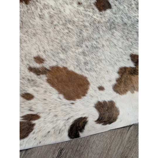 A white and brown extra large cowhide rug with rustic charm and unique characteristics in a natural fluffy texture