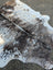 A large cowhide rug with unique characteristics featuring a black white and brown spotted tricolour pattern and rustic charm