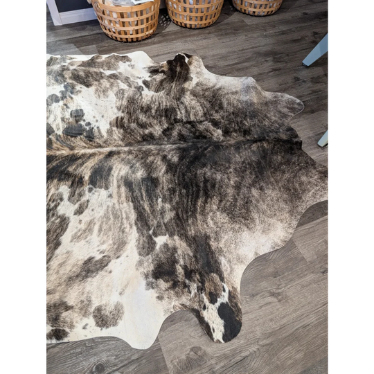 A gorgeous extra large cowhide rug with natural tones and unique rustic charm in white black and brown patches