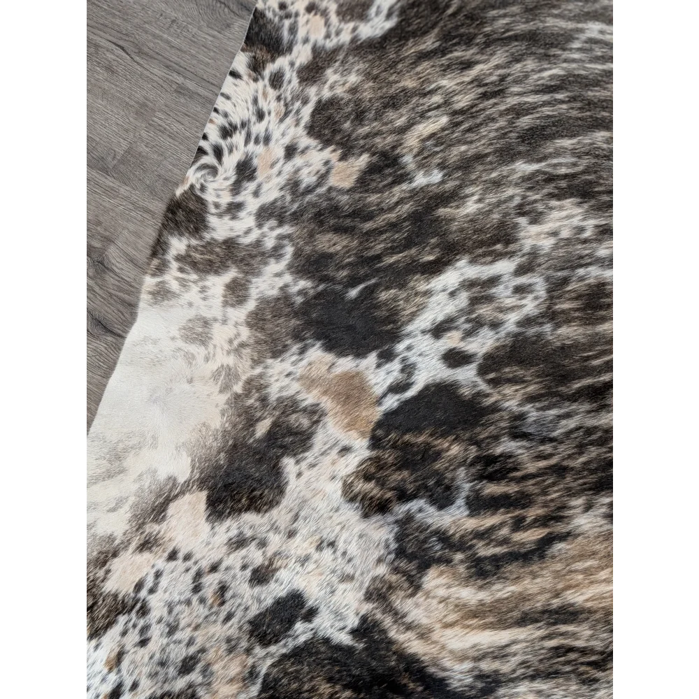 A tricolour 99 extra large cowhide rug with rustic charm featuring mottled black white and tan patches and unique characteristics