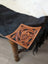 A hand tooled tan leather patch with floral design and black stitched edges on tumbleweed 2 tassel purse with zippered pocket