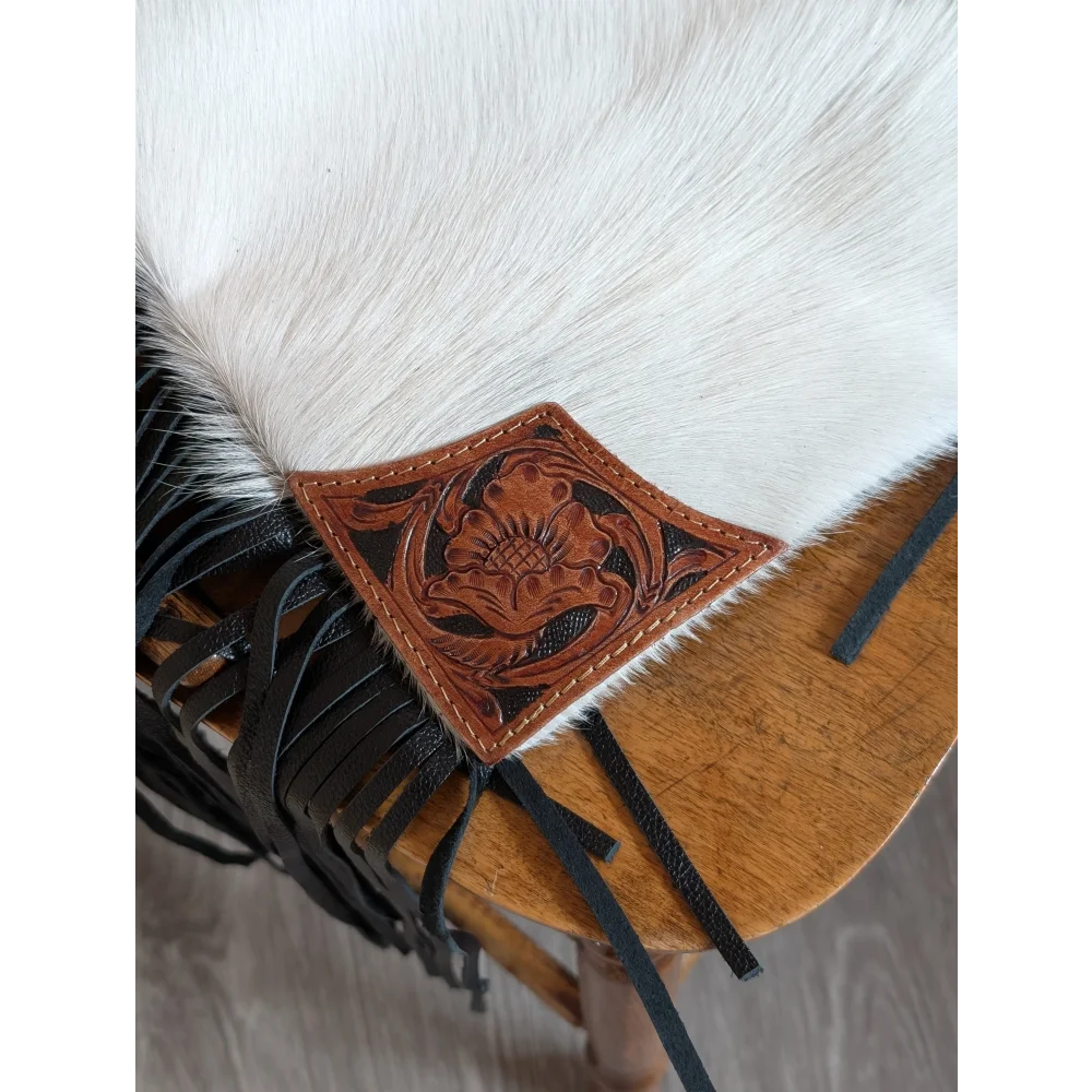 A tan hand tooled leather patch with black stitching on white cowhide for the tumbleweed 4 smoky charcoal tassel purse
