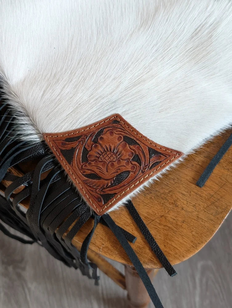 A tan hand tooled leather patch with black stitching on white cowhide for the tumbleweed 4 smoky charcoal tassel purse