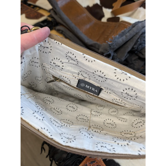 Cream-colored interior lining with subtle black dandelion pattern featuring myra label and gold-toned zipper hardware in tumbleweed 5 tassel purse with zippered pocket and smoky charcoal hand tooled details